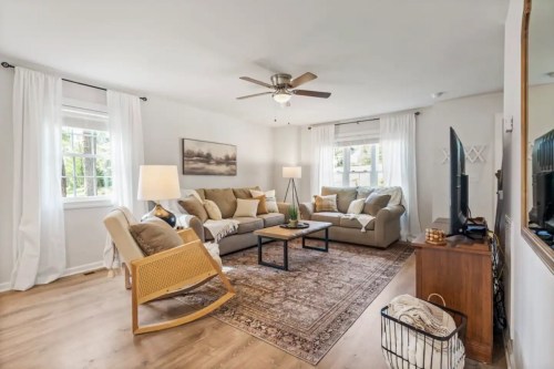 Cozy living room with a sofa, armchair, coffee table, and large windows, featuring light curtains and a warm color palette.
