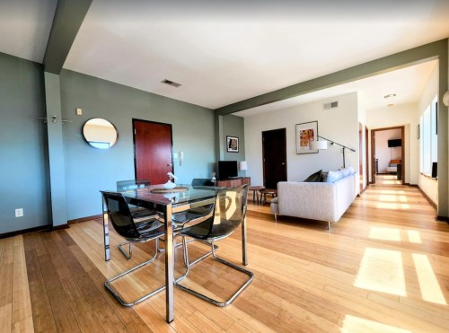 Modern living space featuring a dining area, sofa, and large windows with wooden flooring. Bright and airy atmosphere.