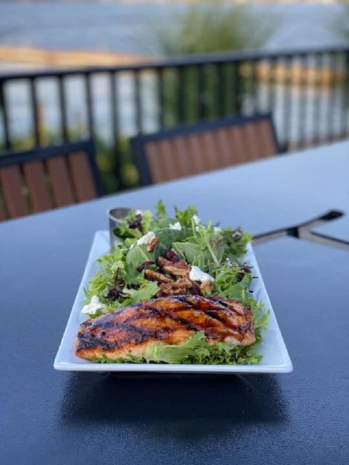 A plate of grilled salmon on a bed of mixed greens, served outdoors with a scenic view in the background.