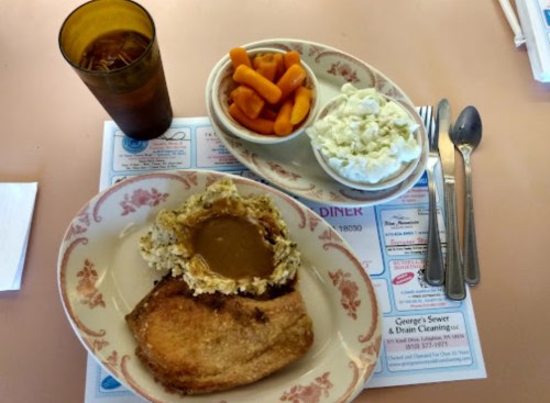 A plate with meatloaf, mashed potatoes with gravy, carrots, and coleslaw, alongside a glass of iced tea.