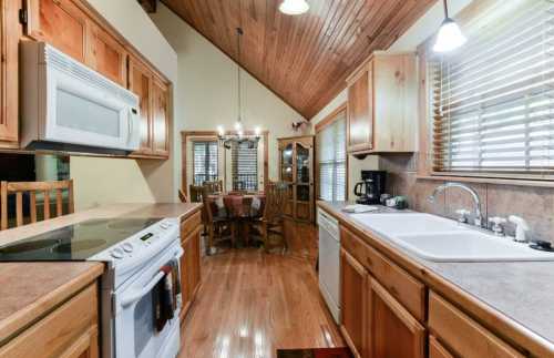 Cozy kitchen with wooden cabinets, a dining area, and a high ceiling featuring exposed beams and warm lighting.