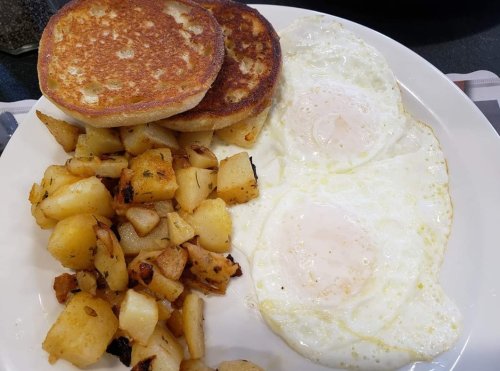 A plate with two fried eggs, golden-brown pancakes, and seasoned diced potatoes.