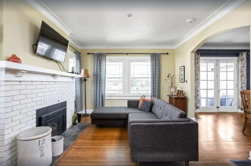A cozy living room featuring a gray sectional sofa, a white brick fireplace, and large windows with blue curtains.