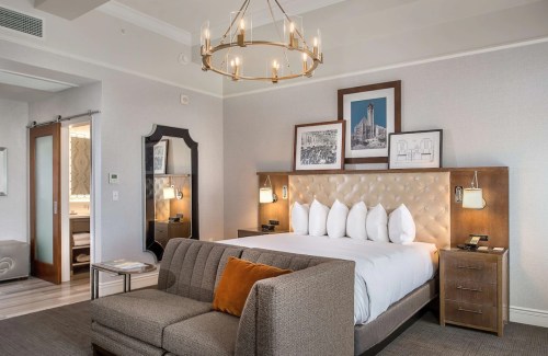 A stylish hotel room featuring a king bed, decorative headboard, sofa, and modern lighting.