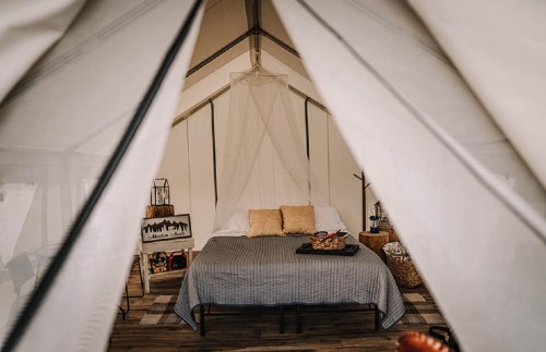 Cozy glamping tent interior featuring a bed, decorative pillows, and a small side table. Warm, inviting atmosphere.