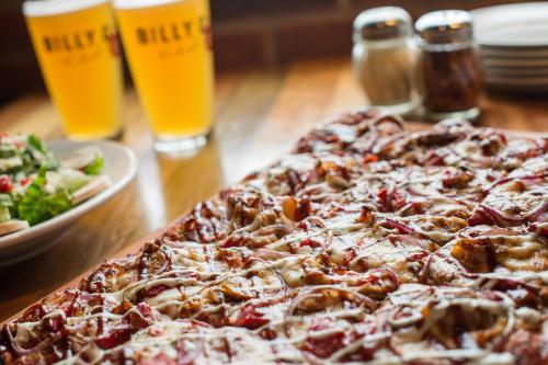 A close-up of a pizza topped with cheese and pepperoni, with two glasses of beer and a salad in the background.