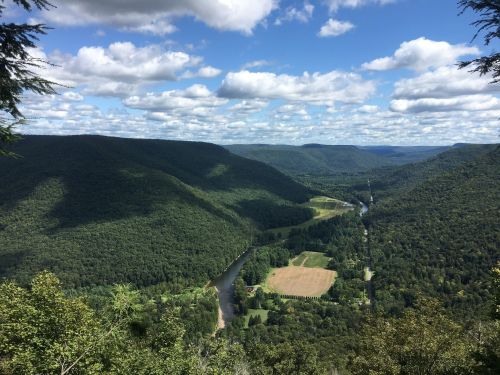 A panoramic view of lush green valleys and a winding river under a partly cloudy sky.