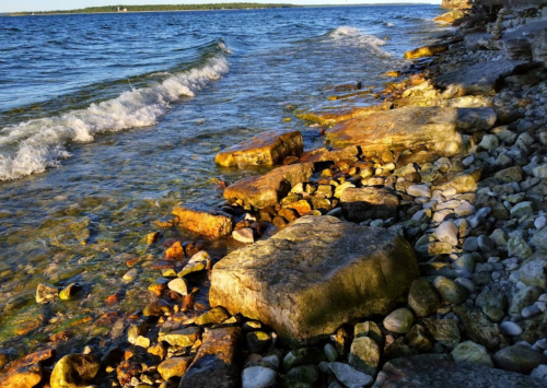 A rocky shoreline with clear water and gentle waves under a bright sky.