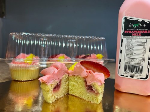 A close-up of a cupcake with pink frosting and a strawberry slice, alongside a bottle of strawberry milk.