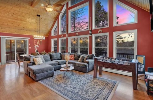Cozy living room with large windows, sunset view, sectional sofa, and foosball table, featuring warm wood accents.