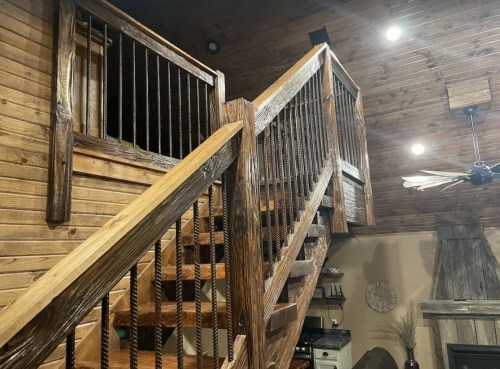 Wooden staircase with rustic railings, leading to a loft area in a cozy, warmly lit interior.