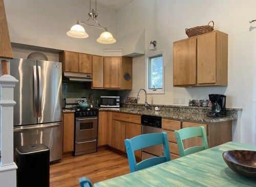 Modern kitchen with wooden cabinets, stainless steel appliances, and a turquoise dining table. Bright and inviting space.