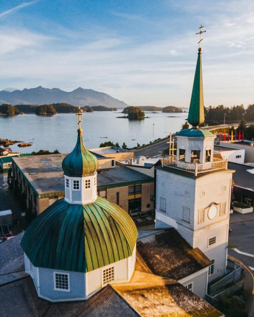 Aerial view of a coastal town with distinctive church towers and mountains in the background, overlooking calm waters.