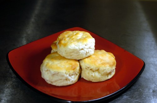 Four golden-brown biscuits stacked on a red plate, resting on a metallic surface.