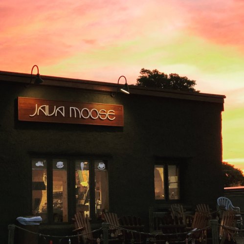 A coffee shop named "Java Moose" with a colorful sunset in the background, featuring outdoor seating.