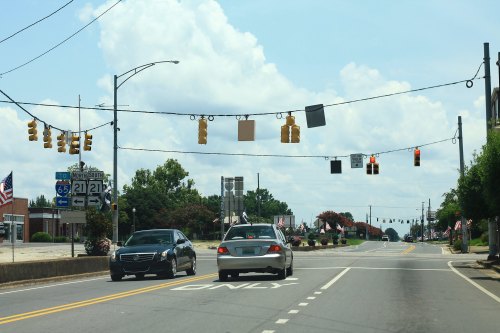 A view of a road with traffic lights, signs, and cars driving under a partly cloudy sky.