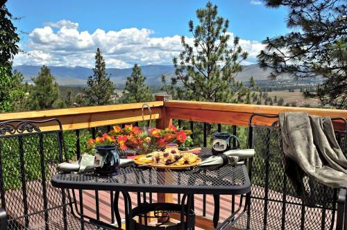 A scenic outdoor dining area with a table set for breakfast, overlooking mountains and trees under a blue sky.