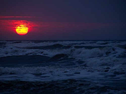 A vibrant sunset casts a warm glow over turbulent ocean waves, creating a dramatic seascape.