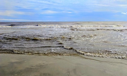 A serene beach scene with gentle waves lapping at the shore under a cloudy blue sky.