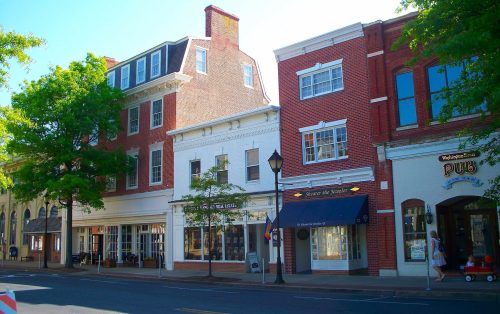 Charming street view featuring brick buildings, shops, and trees under a clear blue sky.