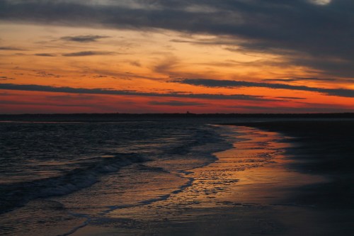 A serene beach at sunset, with waves gently lapping at the shore and vibrant orange and purple clouds in the sky.