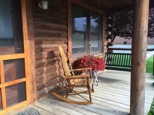 A cozy log cabin porch with a rocking chair and a flower pot filled with red blooms.