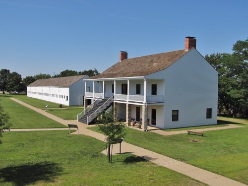 Historic white buildings with porches and a grassy courtyard under a clear blue sky.