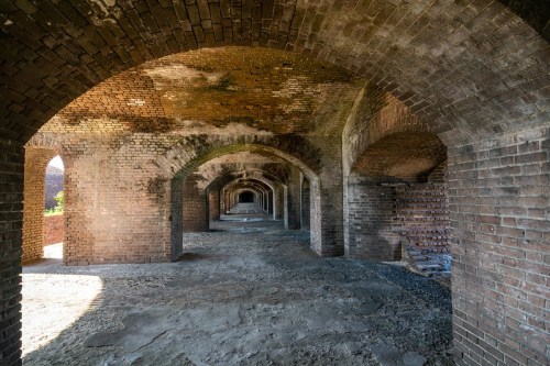 A series of brick arches in an old, abandoned structure, with sunlight illuminating the dusty interior.