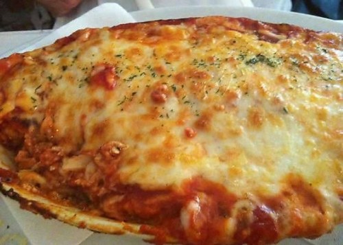 A cheesy, baked lasagna topped with melted cheese and herbs, served in a white dish.