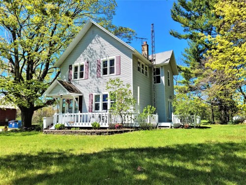 A charming two-story house with a porch, surrounded by green grass and trees on a sunny day.