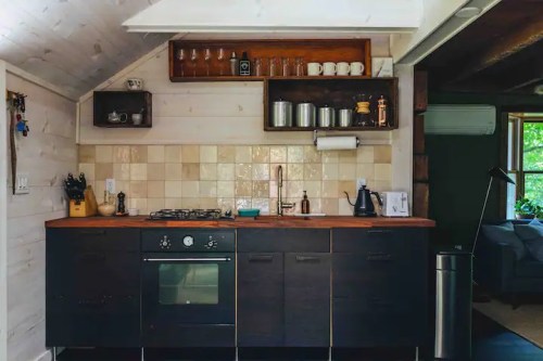 Modern kitchen with dark cabinets, a gas stove, and open shelves displaying glassware and kitchen essentials.