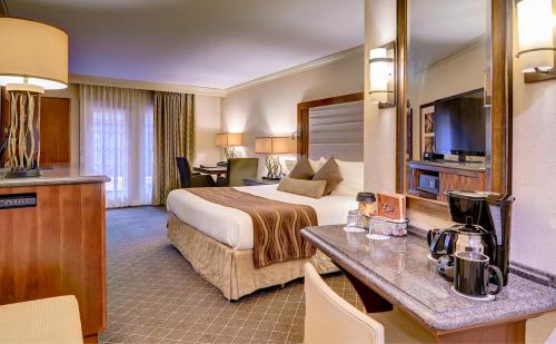 A cozy hotel room featuring a king bed, desk, TV, and coffee station, with warm lighting and modern decor.