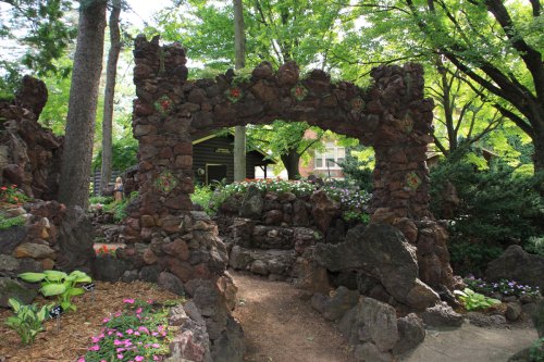 A stone archway surrounded by lush greenery and colorful flowers in a serene garden setting.