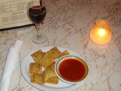 A plate of golden-brown ravioli with marinara sauce, accompanied by a glass of red wine and a lit candle.