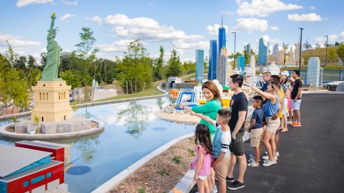 A group of people admire a miniature Statue of Liberty and city skyline at a theme park on a sunny day.