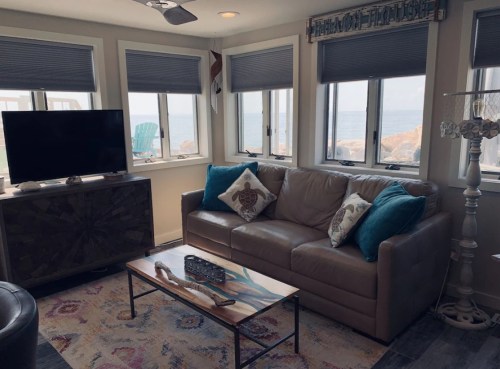 Cozy living room with a leather sofa, decorative pillows, a coffee table, and windows overlooking the ocean.
