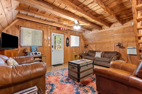 Cozy wooden cabin interior with leather sofas, a coffee table, and a door leading outside. Warm, rustic decor.