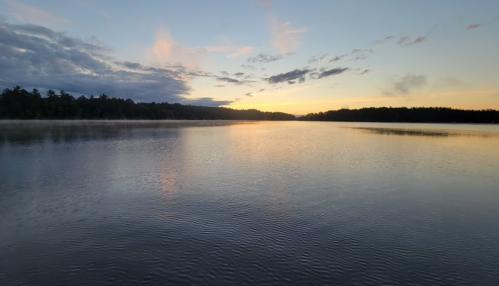 A serene lake at sunset, with soft clouds and a colorful sky reflecting on the calm water.