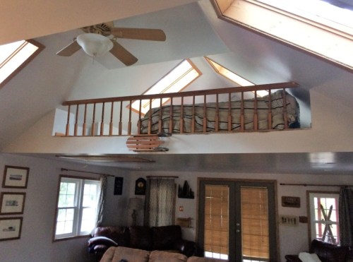A cozy loft with a bed, visible from a living area below, featuring skylights and a ceiling fan.