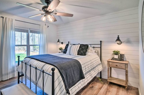 Cozy bedroom with a metal bed, striped bedding, wooden nightstand, and large window letting in natural light.