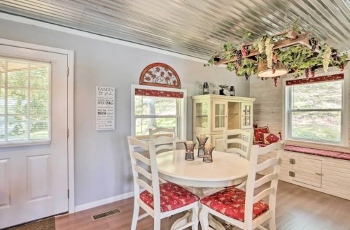 A cozy dining area with a round white table, chairs, and a decorative ceiling, featuring natural light from windows.