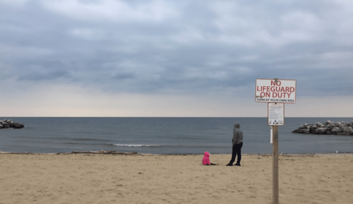 A beach scene with a sign reading "No Lifeguard on Duty," featuring a person and a child near the water.