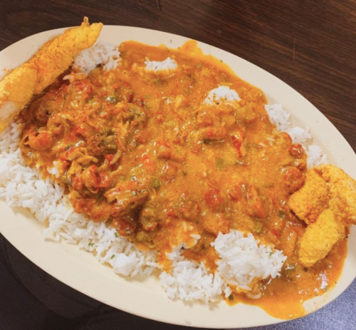 A plate of white rice topped with a rich, orange seafood sauce and two fried shrimp on the side.