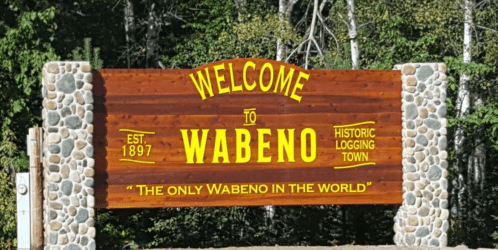 Welcome sign for Wabeno, a historic logging town established in 1897, featuring stone accents and vibrant yellow lettering.