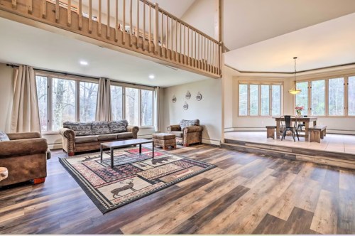 Spacious living area with a rug, sofas, and dining table, featuring large windows and wooden accents.