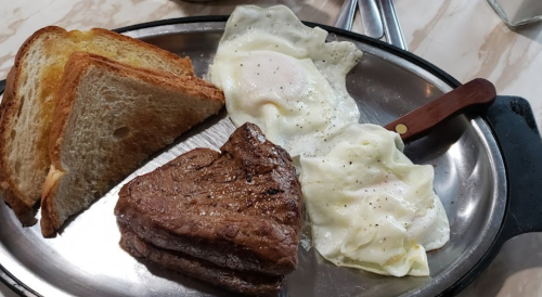 A plate with two fried eggs, a piece of steak, and three slices of toasted bread.
