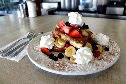 A plate of French toast topped with strawberries, bananas, blueberries, and whipped cream, dusted with powdered sugar.