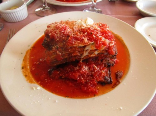 A plate of lasagna topped with marinara sauce and grated cheese, served on a white dish with a pink tablecloth.