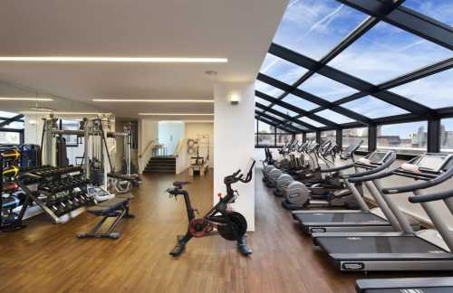 Modern gym with large windows, featuring cardio machines, weights, and a spacious workout area.