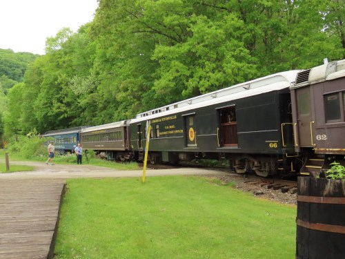 A vintage train parked near a green landscape, with two people walking alongside the tracks.
